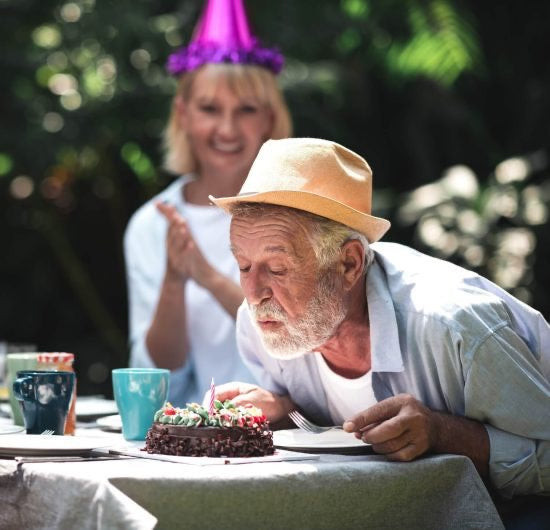 70 year old man blowing out candles on birthday cake