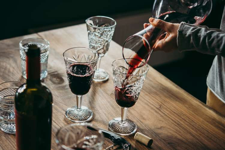 Pouring red wine from a bottle into a glass decanter