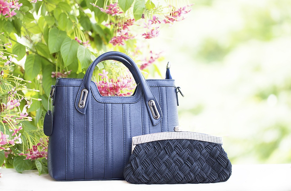 A blue purse with another small bag in front of a tree with pink flowers