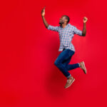 excited man jumping on red background with phone