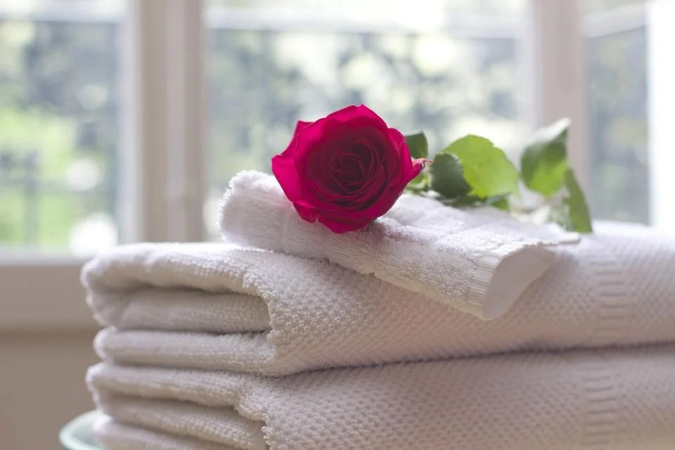 A stack of white bath towels with a rose on top