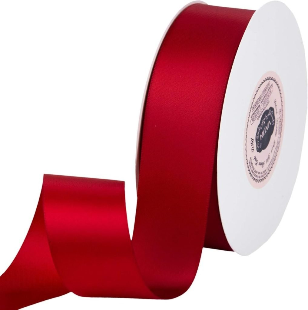 A roll of wide red satin ribbon, perfect for gift wrapping, partially unwound on a white spool, displaying a classic and luxurious ribbon choice.