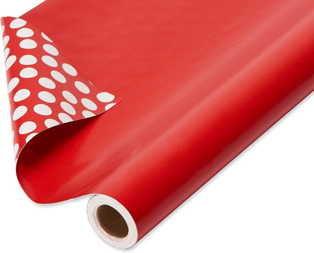A roll of red wrapping paper, perfect for gift wrapping, partially unrolled to reveal a charming white polka dot pattern on the reverse side, highlighting the versatility of reversible gift packaging.
