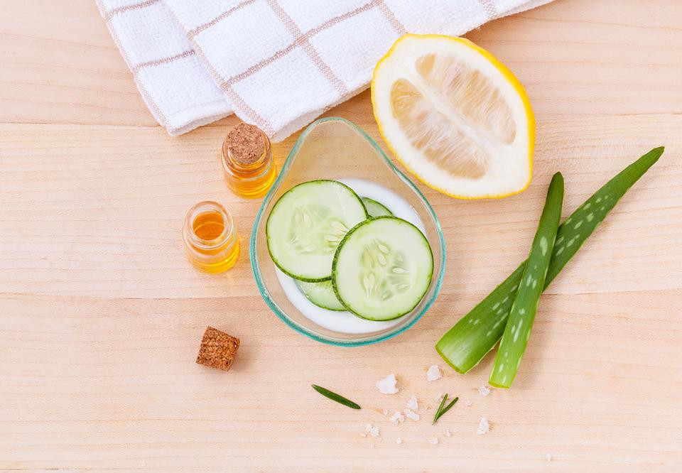 A flat lay photo of a towel, lemon, cucumbers, aloe and honey for a face mask.