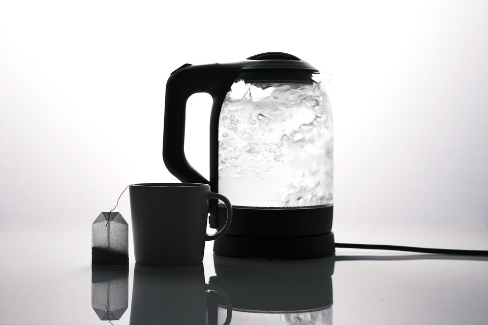An electric kettle boiling water with a mug and tea bag sitting next to it