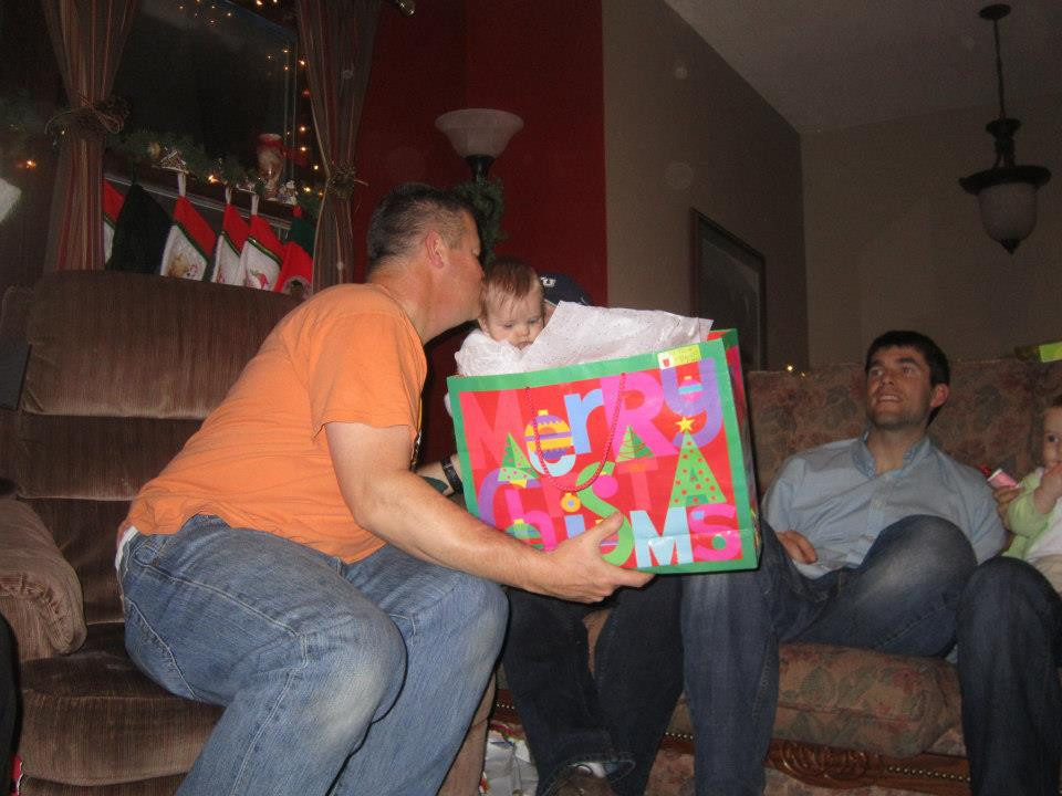 Grandpa gives baby a kiss while he hands her a present for a family Christmas gift exchange