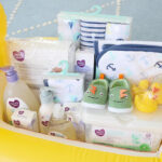 Essential baby items like mattress pad, swaddle blankets, and toiletries arranged in a gift basket.