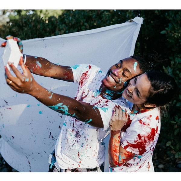A joyful couple with painted smiles taking a selfie using the Adventure Challenge Camera Set, a fun birthday gift for wives.