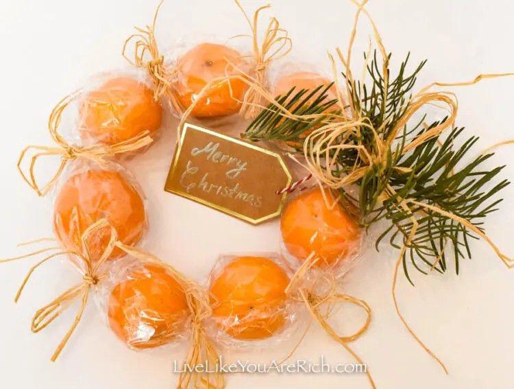 A clementine wreath wrapped in cellophane, showcasing its bright orange color and festive circular shape.