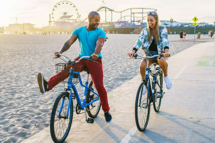 A couple happily cycling along a beach path at sunset, highlighting bicycles as a luxury and active gift idea for married couples.