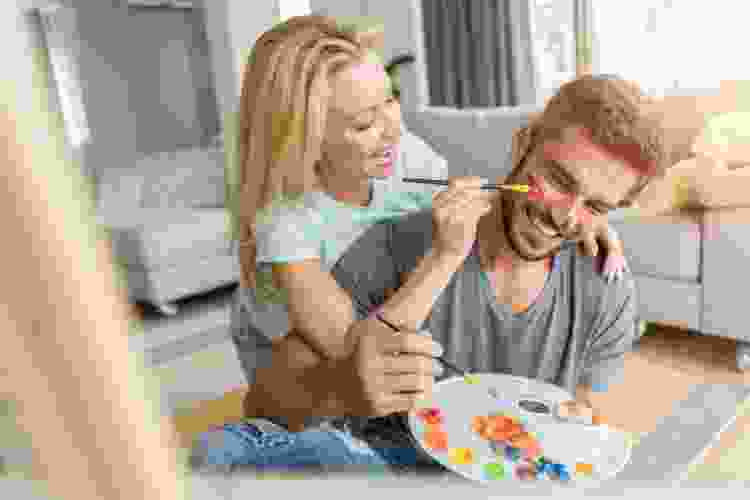 A couple joyfully painting together during a paint and sip class, showcasing a fun and interactive gift idea for married couples.