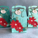 Ombré Christmas gift boxes in Poppy, Nectar, Sea Glass, Tidepool, and Juniper colors, decorated with poinsettias and ribbons.