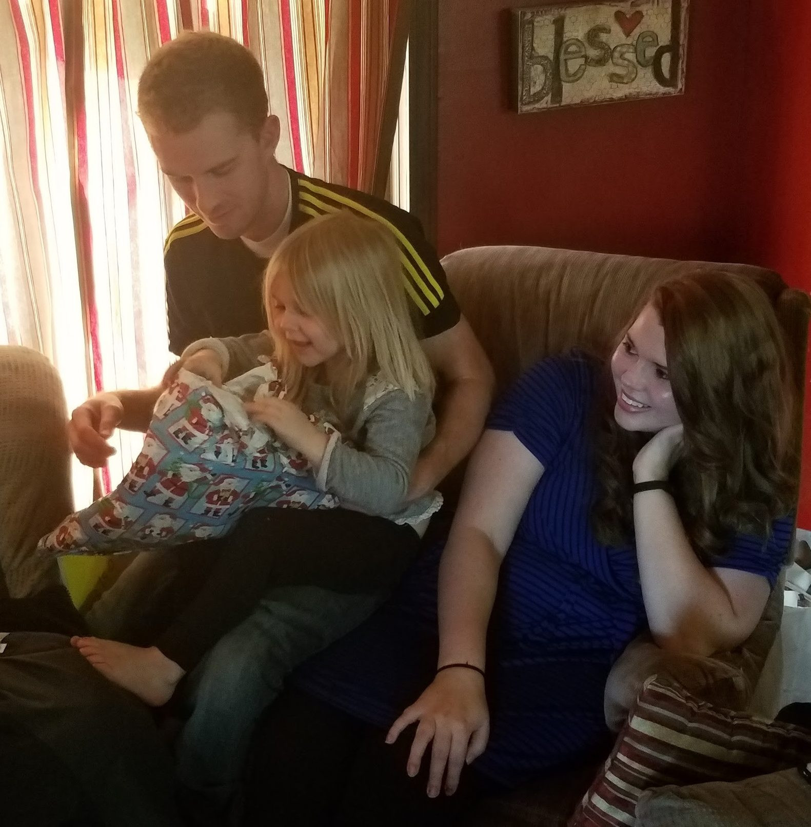Preschooler smiles while uncle gives her a Christmas present and Aunt smiles at the party