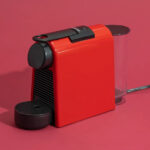 A red Nespresso Essenza Mini on a kitchen counter.