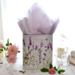 Woman inserting purple tissue paper into a lavender gift bag, enhancing gift presentation