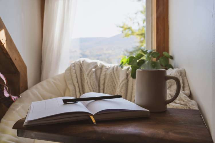 A young woman writing in a personalized journal with an embroidered cover, in a cozy and inspiring setting