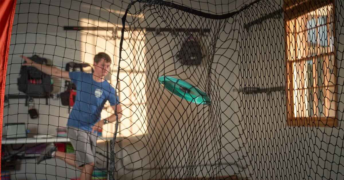 Young man practicing disc golf throws into a net indoors