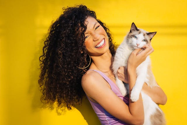 A smiling woman holds a cat close to her face.