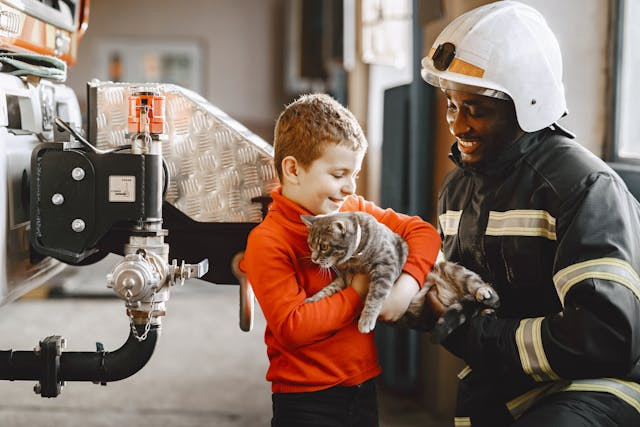 A firefighter hands a cat to a child in a heartwarming scene.
