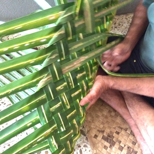 Hands weaving palm leaves into basket