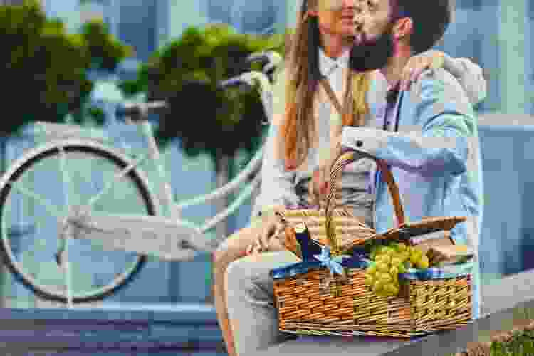 A couple enjoying a picnic on a park bench with a wicker picnic basket, emphasizing the romantic and outdoorsy nature of this gift idea.