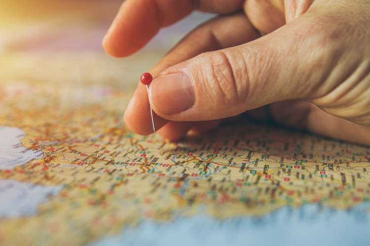 A close-up shot of hands placing colorful push pins into a detailed paper map, symbolizing past travels and future adventures for a married couple.
