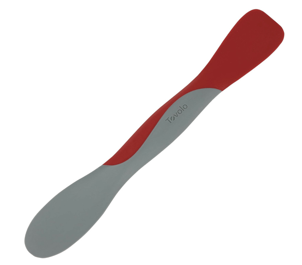 A close-up of a small, red silicone spatula with a wooden handle, showcasing its flexibility and size, perfect for stirring sourdough starter in a jar.