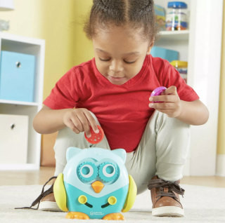A curious toddler interacting with Hoot the Fine Motor Owl, exploring the different shapes and coins that fit into the owl's openings.