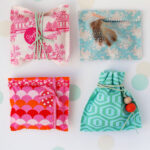 Close-up of handmade fabric gift bags in various pastel colors, tied with ribbons, showcasing a tutorial for crafting charming gift packaging.