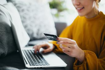 woman sitting on the floor by the sofa, managing financial bill payment with laptop and credit card on hand 